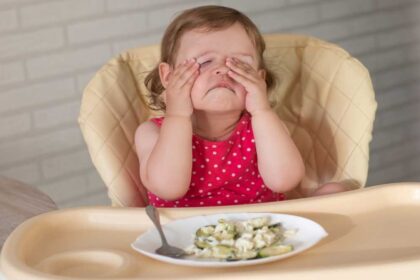 Criança com mãos no rosto e comida na mesa