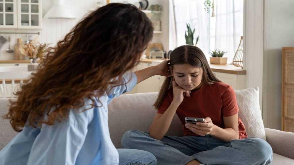Mãe solidária confortando a filha adolescente triste, rejeitada pelos amigos, ajudando a filha deprimida a lidar com o término. Criança adolescente chateada olhando para o celular em casa, esperando uma ligação.