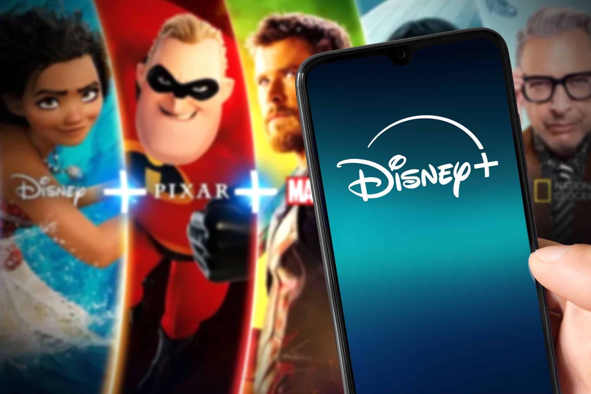 Logo do Disney+ em um smartphone; ao fundo, algumas das atrações oferecidas pelo streaming